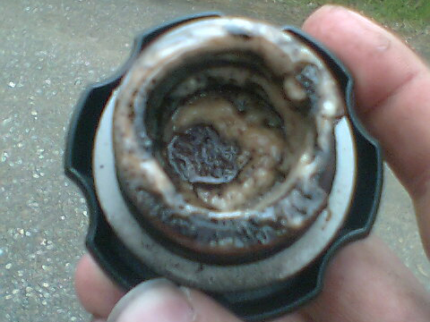 An oil filler cap is held up to show discolouration of the oil.